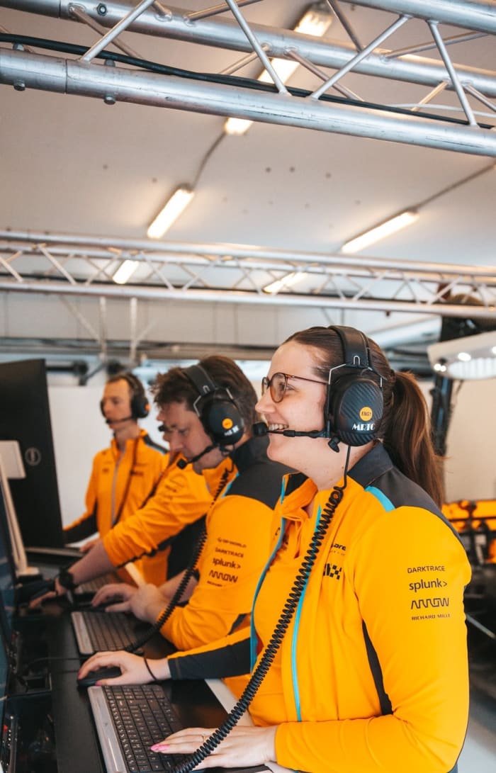 McLaren engineer Amelia Lewis smiles while working alongside colleagues in the F1 team’s garage.